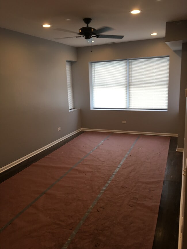 Spacious living room with ceiling fan and four large windows to let in plenty of light. - 7941 S Rhodes Ave
