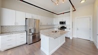 This single-floor space showcases a thoughtful blend of modern finishes and industrial design elements throughout. The open-concept layout connects the kitchen and living areas seamlessly, creating a sense of expansive, flowing space. Exposed ductwork and industrial piping run along the ceilings, adding a distinctive urban character that contrasts stylishly with the clean white walls and warm wood-look flooring.

The kitchen is a standout feature, equipped with crisp white shaker cabinetry extending to the ceiling, granite countertops, and a classic subway tile backsplash. A central island with a built-in sink provides additional prep space and casual seating. Stainless steel appliances, including a French door refrigerator, gas range, and microwave, complete the well-equipped cooking space.

The living area benefits from a wall of oversized windows fitted with vertical blinds, flooding the space with natural light and offering outdoor views. Exposed silver ductwork carries the industrial aesthetic into this room as well.

Two bathrooms serve the unit. The primary bathroom features a glass-enclosed walk-in shower, a grey vanity with granite countertop, a lighted mirror, and wood-look tile flooring. The secondary bathroom offers a similarly styled vanity with granite countertop, a well-lit mirror, and matching tile flooring, providing a cohesive aesthetic throughout.