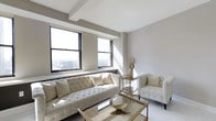 Situated in the heart of downtown Columbus, Ohio, this single-floor space at 50 W Broad St offers an elevated urban living experience with striking panoramic views of the city skyline. The interior is characterized by a refined, contemporary aesthetic, with a neutral color palette of crisp whites and soft grays that creates a clean, airy atmosphere throughout.

The living area is a standout feature, anchored by large black-framed windows that flood the space with natural light and frame impressive elevated views of the Columbus cityscape. The room is appointed with elegant tufted seating in ivory tones, accented by gold and glass furnishings that add a luxurious, sophisticated touch. Exposed structural beams along the ceiling contribute an architectural detail that complements the modern design sensibility.

The overall ambiance of the space is bright, open, and polished, blending classic elegance with contemporary urban style. Its prime downtown location provides easy access to Columbus's business district, dining, entertainment, and cultural destinations, making it an ideal setting for both professional and personal use.