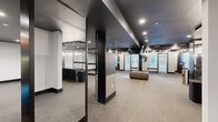 This expansive fitness center offers a thoughtfully designed, single-floor layout that caters to a wide range of exercise disciplines. The space is defined by its striking design aesthetic — bold black ceilings contrast with crisp white walls, while carpeted flooring and recessed lighting create a refined, gym-like ambiance throughout.

The main open exercise floor is generously proportioned, providing ample room for stretching, group classes, or cardio equipment. Adjacent to this area is a dedicated ballet barre studio, enclosed by full-length glass panels framed in dark trim. Floor-to-ceiling mirrors line the walls, enhancing both the sense of space and functionality for barre and dance-inspired workouts.

A separate strength and functional training zone houses a multi-functional cable machine, resistance equipment, medicine balls, agility tools, and other functional fitness accessories. Cardio equipment, including treadmills, is visible near the windows along the perimeter, which admit natural light through louvered blinds.

The reception or check-in area near the entrance features an elegant marble-topped counter with pendant lighting, adding a polished, upscale touch. Multiple private rooms and restroom facilities are accessible via a corridor, rounding out the comprehensive amenities. Throughout the space, the design balances high-end aesthetics with practical fitness functionality.