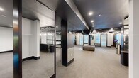 This expansive fitness center offers a thoughtfully designed, single-floor layout that caters to a wide range of exercise disciplines. The space is defined by its striking design aesthetic — bold black ceilings contrast with crisp white walls, while carpeted flooring and recessed lighting create a refined, gym-like ambiance throughout.

The main open exercise floor is generously proportioned, providing ample room for stretching, group classes, or cardio equipment. Adjacent to this area is a dedicated ballet barre studio, enclosed by full-length glass panels framed in dark trim. Floor-to-ceiling mirrors line the walls, enhancing both the sense of space and functionality for barre and dance-inspired workouts.

A separate strength and functional training zone houses a multi-functional cable machine, resistance equipment, medicine balls, agility tools, and other functional fitness accessories. Cardio equipment, including treadmills, is visible near the windows along the perimeter, which admit natural light through louvered blinds.

The reception or check-in area near the entrance features an elegant marble-topped counter with pendant lighting, adding a polished, upscale touch. Multiple private rooms and restroom facilities are accessible via a corridor, rounding out the comprehensive amenities. Throughout the space, the design balances high-end aesthetics with practical fitness functionality.