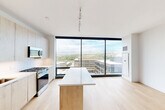 This modern 1-bedroom, 1-bathroom unit in Boise, Idaho offers a thoughtfully designed open-concept layout with a bright, contemporary aesthetic throughout. The combined living, dining, and kitchen area serves as the heart of the home, anchored by dramatic floor-to-ceiling windows that flood the space with natural light and frame sweeping views of the Boise cityscape and surrounding mountain range. Light hardwood flooring runs throughout the main living areas, complementing the clean, minimalist design.

The kitchen is well-appointed with light wood cabinetry extending to the ceiling, stainless steel appliances including a gas range, microwave, dishwasher, and refrigerator, a white quartz countertop, and a central island with a matching wood-accented base — ideal for dining or meal prep. Track lighting overhead adds a modern industrial touch.

The bedroom is a bright, serene retreat with its own access to the expansive windows and views, and features a standout exposed concrete column — a striking architectural detail. The bathroom offers a dual-sink vanity with light wood cabinetry, white quartz countertops, brushed gold fixtures, and a large backlit mirror. Additional conveniences include in-unit laundry and multiple closets for ample storage.