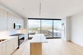 This modern 1-bedroom, 1-bathroom unit in Boise, Idaho offers a thoughtfully designed open-concept layout with a bright, contemporary aesthetic throughout. The combined living, dining, and kitchen area serves as the heart of the home, anchored by dramatic floor-to-ceiling windows that flood the space with natural light and frame sweeping views of the Boise cityscape and surrounding mountain range. Light hardwood flooring runs throughout the main living areas, complementing the clean, minimalist design.

The kitchen is well-appointed with light wood cabinetry extending to the ceiling, stainless steel appliances including a gas range, microwave, dishwasher, and refrigerator, a white quartz countertop, and a central island with a matching wood-accented base — ideal for dining or meal prep. Track lighting overhead adds a modern industrial touch.

The bedroom is a bright, serene retreat with its own access to the expansive windows and views, and features a standout exposed concrete column — a striking architectural detail. The bathroom offers a dual-sink vanity with light wood cabinetry, white quartz countertops, brushed gold fixtures, and a large backlit mirror. Additional conveniences include in-unit laundry and multiple closets for ample storage.