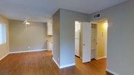 This single-floor space offers a clean and functional layout designed for comfortable everyday living. The interior is finished with warm hardwood-style flooring that runs throughout, complementing the neutral gray wall tones and crisp white trim that give the space a bright, cohesive feel.

The open-plan living and kitchen area forms the heart of the unit. The kitchen is equipped with white cabinetry, a light-toned countertop, a built-in dishwasher, a refrigerator, and a sink, all arranged efficiently along one wall. A peninsula or dividing column separates the kitchen from the adjacent living area, adding architectural definition while maintaining an open, airy atmosphere. A ceiling fan with integrated lighting fixture is centrally positioned overhead, providing both air circulation and ambient illumination.

Additional features include a built-in shelving unit or linen closet near the entryway, offering convenient storage. A visible HVAC vent in the ceiling ensures climate control throughout the space. The layout flows naturally between areas, making the most of the available footprint. Overall, the space presents a practical and well-maintained interior with a neutral palette that lends itself easily to a variety of furnishing styles.