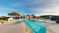 This outdoor amenity facility is centered around a large, resort-style swimming pool with clearly marked lap lanes and a surrounding concrete deck lined with lounge chairs — ideal for relaxing under open skies. Mature trees and palm accents frame the pool area, contributing to a lush, welcoming atmosphere. A fenced perimeter ensures privacy and security throughout the space.

Adjacent to the pool, a covered pavilion provides a comfortable shaded retreat for outdoor dining and socializing. The pavilion features a striking vaulted shiplap ceiling with multiple ceiling fans for airflow, large open-air windows that invite natural light and outdoor views, and spacious tile flooring accommodating multiple dining tables and chairs.

The interior support space is clean and modern, featuring large-format tile flooring, crisp white cabinetry with stainless steel countertops, and bright recessed lighting. This area connects seamlessly to a dedicated pet wash station, which is equipped with stainless steel tub surrounds, abundant natural light from multiple windows with horizontal blinds, and tiled floors — a practical and thoughtfully designed amenity. A full bathroom rounds out the facility, providing convenience for guests enjoying the outdoor amenities.
