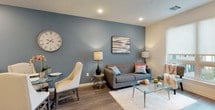 This well-appointed single-floor residence showcases a thoughtfully designed open-concept layout with modern finishes throughout. The kitchen is a standout feature, equipped with stainless steel appliances—including a gas range, built-in microwave, and refrigerator—complemented by crisp white shaker cabinetry, a mosaic tile backsplash, and dark countertops. A peninsula with bar seating provides both additional prep space and a casual dining option. Wood-look plank flooring flows seamlessly from the kitchen into the combined living and dining area, which is anchored by a striking slate-blue accent wall. Large windows invite natural light and offer exterior views, creating a bright and welcoming atmosphere. The space accommodates both a dining set and a comfortable living arrangement with ease. Two bedrooms provide restful retreats; one features oversized windows with roller shades and soft neutral tones, while the second includes warm accent walls, double closets, and ample storage. The bathroom is finished to a high standard, with marble-look tile flooring, a backlit vanity mirror, white cabinetry with a gray countertop, and a combination tub and shower with tiled surround. The overall aesthetic is clean, contemporary, and cohesive throughout.
