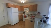 This two-floor residence offers a practical and comfortable layout designed to meet everyday living needs. The kitchen serves as a functional centerpiece, featuring warm honey-toned wood cabinetry that provides ample storage space both above and below the counters. Light-toned laminate countertops complement the cabinetry, while the full suite of white appliances — including a refrigerator, electric range, over-the-range microwave, and a double basin sink — ensures all essential culinary needs are met. A peninsula-style counter extension adds additional workspace and can serve as a casual dining or prep area. The kitchen flows naturally into the adjacent living areas, creating an open and connected feel. Hardwood-style flooring runs throughout the kitchen, adding warmth and ease of maintenance to the space. Ceiling-mounted lighting provides consistent illumination across the kitchen. Spanning two floors, the residence offers a clear separation between living and private spaces, making it well-suited for a variety of lifestyles. The overall design balances functionality with a welcoming, neutral aesthetic that provides a versatile canvas for personal style.