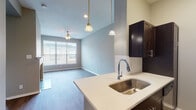 Located at 210 N Crowdus St in Dallas's vibrant Deep Ellum neighborhood, this single-floor residence offers a thoughtfully designed open-concept layout finished with warm, neutral tones and wood-look flooring throughout. The living area serves as the centerpiece of the home, anchored by a classic white-mantled fireplace with tile surround and soaring accent walls that lend a sense of height and openness. Built-in shelving along one wall provides both functional storage and a distinctive architectural detail.

The kitchen is well-appointed with dark espresso cabinetry, a white quartz peninsula countertop featuring an undermount sink, subway tile backsplash, and a full suite of stainless steel appliances including a refrigerator, range, and built-in microwave. Pendant lighting above the peninsula adds a polished, contemporary touch. The kitchen flows seamlessly into a bright dining area illuminated by additional pendant fixtures and a large window that draws in natural light.

The bedrooms are comfortably sized, each featuring ceiling fans, neutral walls, and generous windows fitted with blinds. The bathroom includes a soaking tub with tiled surround and chrome fixtures. Ceiling fans are present throughout, contributing to the home's practical and comfortable atmosphere.