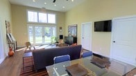 The community space at Lakewood Park Apartments is thoughtfully designed to offer residents a comfortable and functional gathering area. The single-floor layout features soaring ceilings that amplify the sense of openness, complemented by large floor-to-ceiling windows and glass-paned French doors that flood the interior with natural light and provide pleasant views of the surrounding green landscape outside.

The lounge area is furnished with a substantial dark sofa and modern blue accent chairs arranged around a sleek glass-top table, creating an inviting space for socializing or relaxing. A wall-mounted flat-screen television is positioned prominently for easy viewing. A dark wood storage credenza adds both style and practicality to the room, while decorative plants introduce a touch of nature indoors.

Recessed ceiling lighting, paired with a ceiling fan, ensures the space remains well-lit and comfortable throughout the day and evening. Warm, neutral-toned walls contribute to a calm, welcoming ambiance. The hardwood-style flooring anchors the space with warmth and durability. Together, these elements create a polished yet approachable communal environment that reflects the overall character of Lakewood Park Apartments.