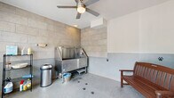 Located at 1824 Defoor Ave NW in Atlanta, GA, this single-room pet grooming suite is thoughtfully designed for professional use. The space is anchored by a large, commercial-grade stainless steel grooming tub, complete with an integrated ramp, handheld sprayer, and restraint hooks — providing a fully equipped bathing station for pets of all sizes. Large-format stone-look tile cladding covers the lower half of the walls, extending fully on the wet area surround, offering both a polished aesthetic and easy-to-clean functionality. The durable speckled epoxy floor is both practical and visually cohesive, adorned with decorative paw print motifs that add a playful character to the room. A ceiling fan overhead ensures comfortable air circulation during grooming sessions. Natural light enters generously through a large window and a glass-panel entry door, offering views of the surrounding greenery and keeping the space bright and welcoming. A wooden bench provides a convenient seating area, while wire shelving along one wall keeps grooming supplies neatly organized and within reach. A floor drain is centrally positioned for efficient cleanup. The overall design strikes a balance between professional utility and an inviting atmosphere tailored for a pet-friendly environment.