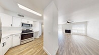 This single-floor residence offers a clean, modern aesthetic defined by a consistent palette of white walls, crisp trim, and wood-look tile flooring that runs throughout the entire space. The open-concept living area is generously proportioned, anchored by a fireplace set against a painted white brick accent wall, and fitted with a ceiling fan overhead. Natural light filters in through blinded windows, enhancing the bright and airy atmosphere. A pass-through counter connects the living area to the kitchen, which features white shaker-style cabinetry with matte black hardware, white quartz countertops, and a full suite of stainless steel appliances including a range, over-the-range microwave, and built-in lighting. The bedrooms continue the home's cohesive design, each showcasing the white brick accent walls, ceiling fans, and windows that invite natural light. At least one bedroom includes a walk-in closet, providing practical storage. The bathroom is well-appointed with a white vanity topped with a solid surface countertop, a large mirror, brushed gold hardware accents, and a painted brick wall that adds texture and character. The shower area features clean, bright surrounds and wood-look tile flooring, maintaining a unified look across the home.