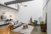 Unit 1106 at 11900 Main St in Fredericksburg, Virginia is a two-story residence that blends modern finishes with industrial character. The main living area immediately impresses with dramatically soaring ceilings, exposed ductwork overhead, and polished concrete floors that lend an urban, loft-like aesthetic. A staircase connects the two levels, and the open layout creates a generous, airy sense of space throughout the main floor.

The kitchen is well-appointed with gray shaker-style cabinetry, a white subway tile backsplash, stainless steel appliances, and granite countertops. A large kitchen island with seating for multiple guests serves as both a functional workspace and a casual dining area, illuminated by pendant lighting above.

Upstairs, the bedroom features light wood flooring, soaring walls painted in crisp white, and bold dark-trimmed doors that create a striking contrast. The bedroom connects directly to a full bathroom, which is finished with large-format white tile surrounding a soaking tub and shower combination. A convenient powder room is also available, featuring granite countertop accents and clean, neutral finishes. Throughout the unit, the consistent use of modern materials, high ceilings, and a neutral color palette creates a cohesive and contemporary living environment.