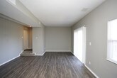 This single-floor residence offers a thoughtfully arranged layout with a variety of finishes throughout. The living area is a generously sized, open space featuring dark hardwood-style flooring and neutral gray walls, with a sliding glass door and an additional window allowing natural light to fill the room and providing views to the outdoors. A subtle step-down transition leads toward the entryway, adding a subtle architectural detail to the space.

The kitchen is well-equipped and features rich dark espresso cabinetry paired with light countertops and a white subway tile backsplash. Black appliances, including a refrigerator, gas range, and dishwasher, complement the cabinetry, while warm-toned hardwood-style flooring ties the space together. A flush-mount ceiling light provides ample overhead illumination.

The bedrooms are carpeted in a neutral tone and each include a sliding-door closet with built-in shelving, offering practical storage. Gray walls and textured ceilings carry throughout these rooms consistently.

The bathroom features dark hardwood-style flooring, a full-sized soaking tub with a white tiled surround, a curved shower rod, and brushed nickel fixtures and grab bar, delivering a clean and functional design.