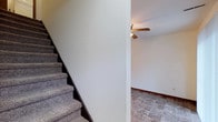 This two-floor home offers a straightforward and functional layout designed for everyday living. The main level is anchored by durable stone-tile flooring in a natural, earthy palette, providing both practicality and a grounded aesthetic throughout the space. A ceiling fan is installed overhead, ensuring year-round comfort and air circulation. Crisp white walls reflect light throughout the interior, contributing to a clean and open atmosphere. A carpeted staircase with dark wood framing connects the main level to the upper floor, serving as a central transition point between the two stories. The dark baseboards running along the lower walls add a subtle contrast to the light-toned walls, lending the space a defined, finished look. The overall design of this home is simple and unassuming, prioritizing comfort and usability. With two full floors of living space, there is ample room for flexible arrangements and a variety of living needs. The neutral finishes and practical materials throughout make this a versatile home, well-suited for a range of styles and uses.