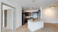 This single-floor residence offers two bedrooms and two bathrooms within a thoughtfully designed open layout. The kitchen serves as a focal point, featuring dark espresso cabinetry with ample storage, light granite countertops, and a subway tile backsplash that adds a clean, contemporary touch. Stainless steel appliances, including a refrigerator, microwave, and range, provide a cohesive and functional cooking environment. A peninsula with a granite surface and an integrated sink extends into the living area, creating a natural transition between the kitchen and the broader living space while offering additional seating and prep space. Track lighting overhead ensures the kitchen is well-lit and practical. The flooring transitions from wood-style planks in the kitchen to carpet in the living areas, adding warmth and comfort underfoot. The open-concept design allows natural light to flow throughout, enhancing the airy feel of the space. Neutral wall tones and a textured ceiling complement the modern finishes, creating a balanced and inviting ambiance throughout this well-sized home.