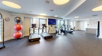 This state-of-the-art fitness facility, located at 1 Canal in Boston, MA, spans 1,970 square feet on a single floor. The space is expertly designed to accommodate various workout styles, with a particular focus on yoga and spinning classes. The gym boasts a modern, open-concept layout with high ceilings and large windows that flood the area with natural light, offering stunning views of the Boston cityscape.

The facility is equipped with a comprehensive range of exercise machines, including treadmills, stationary bikes, ellipticals, and weight training equipment. Specialized areas are designated for yoga and spinning, ensuring ample space for group classes. The flooring is a durable, shock-absorbing material ideal for high-impact activities.

Thoughtful lighting design incorporates both recessed and large circular ceiling fixtures, creating a bright, energizing atmosphere. Wall-mounted televisions and mirrors are strategically placed throughout the space, enhancing the workout experience. Additional amenities include storage areas for personal belongings and equipment, contributing to the gym's clean, uncluttered appearance.

The overall ambiance is one of contemporary sophistication, blending functionality with aesthetic appeal to create an inviting environment for fitness enthusiasts of all levels.