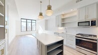 Located in the heart of Atlanta's Midtown neighborhood at 770 Juniper St NE, this thoughtfully designed single-floor residence combines contemporary aesthetics with functional living. The open-concept kitchen serves as a central highlight, featuring sage-toned shaker cabinetry with brushed brass hardware, a crisp white subway tile backsplash, quartz countertops, and a generously sized island with built-in open shelving. Stainless steel appliances, including a gas range, microwave, and refrigerator, complete the chef-ready space. Statement pendant lights with a brass and frosted glass finish add warmth overhead. Large floor-to-ceiling windows flood the living area with abundant natural light and frame impressive panoramic views of the Atlanta skyline. Light wood-toned flooring runs throughout, complementing the clean white walls and creating a bright, airy atmosphere. The bedrooms are well-proportioned and sun-drenched, each benefiting from the same expansive city views. The entryway features a practical built-in mudroom with open shelving, coat hooks, and a bench. The bathroom is finished with large-format tile flooring, white cabinetry with brass accents, a walk-in glass shower, and a well-appointed vanity, delivering a polished, spa-like feel.