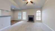 This single-story residence is designed with an open, functional layout that connects the main living spaces seamlessly. The living room serves as the centerpiece of the home, featuring vaulted ceilings that enhance the sense of height and openness. A ceiling fan with a light fixture is centrally mounted, providing both airflow and ambient lighting. A gray tile-surround fireplace anchors one wall, flanked by a rear-access door and multiple windows, including a distinctive arched window that allows generous natural light to fill the room. Neutral carpet covers the living and bedroom floors, while wood-look flooring extends through the kitchen and bathroom areas.

The galley-style kitchen includes dark cabinetry with granite-style countertops, stainless steel appliances, and a pass-through breakfast bar that connects to the living area. Built-in shelving near the hallway provides additional storage and display space. The bedrooms are well-proportioned, each equipped with ceiling fans and arched or standard windows that bring in natural light. The bathroom features a full tiled tub-shower combination, wood-look flooring, and clean white fixtures. Overall, the home presents a cohesive, neutral aesthetic throughout.