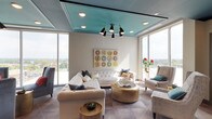 Located at 985 N High St in Columbus, Ohio, this sophisticated amenity lounge at Eight on High is a striking communal space designed with a keen eye for contemporary elegance. The space is defined by its signature teal-painted ceilings, which add a bold, cohesive visual identity throughout, from the welcoming entry corridor to the expansive main lounge area.

The entry area greets visitors with a herringbone-patterned wood accent wall, geometric tile flooring, and gold-lettered "EIGHT" signage, setting an upscale tone. A stylish console table with decorative greenery and dual elevator bays with polished stainless steel doors and a wood veneer surround complete the refined arrival experience.

The main lounge opens dramatically with floor-to-ceiling windows wrapping around multiple walls, flooding the space with natural light and offering panoramic views of the Columbus skyline and surrounding neighborhoods. The seating areas are thoughtfully arranged, featuring tufted white sectional sofas, plush velvet accent chairs, and brushed gold coffee tables. A sculptural multi-arm chandelier anchors one seating vignette beneath a coffered teal ceiling detail. Colorful circular artwork adds a vibrant focal point to the neutral palette. The geometric tile flooring carries throughout, unifying the entire space with a modern, polished aesthetic.