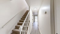 Located at 110 Village Park Dr in Simpsonville, SC, this two-story home offers 3 bedrooms and 2 bathrooms spread evenly across two floors. The layout is thoughtfully organized, with each level contributing equally to the overall living space.

The kitchen is a standout feature, outfitted with crisp white shaker cabinets, granite-look countertops, a black-hardware sink, and a full suite of stainless steel appliances including a refrigerator, range, microwave, and dishwasher. Light wood-style flooring runs through the kitchen and main living areas, giving these spaces a clean, contemporary feel.

A carpeted staircase with white-painted railings connects the two floors, flanked by a bright hallway that leads toward a rear door with natural light filtering through. The bedrooms are carpeted throughout and feature neutral walls, ceiling fans in select rooms, and windows dressed with blinds that allow natural light while maintaining privacy. The primary bedroom includes a closet with shelving. Additional bedrooms are compact yet functional, each with exterior-facing windows.

The bathrooms are finished in clean white with tub-shower combinations and wood-style flooring. A dedicated laundry area includes built-in upper shelving and washer/dryer hookups. A hallway closet provides additional storage.