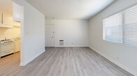 Located on Cornuta Ave in Bellflower, California, this single-story, one-bedroom, one-bathroom unit offers an efficient and well-organized layout. The living room serves as the central gathering space, featuring light-toned luxury vinyl plank flooring, crisp white walls, a textured ceiling, and a front entry door. A wall-mounted heating unit provides climate control, while a window dressed with horizontal blinds allows natural light to filter in.

The galley-style kitchen is positioned adjacent to the living area and is outfitted with white cabinetry offering ample storage, a double-basin sink, a gas range, and a dedicated space for a refrigerator. The light LVP flooring continues seamlessly throughout.

The bedroom is a comfortable, well-proportioned room with plush carpeting, white walls, and a window with blinds that brings in natural light. It connects directly to the hallway, which provides access to the bathroom.

The bathroom features full-height ceramic tile surrounding a soaking tub with an overhead shower, a white vanity with sink, and a mirrored medicine cabinet — all finished in a clean, neutral palette.

Throughout the unit, the consistent use of white tones and light flooring creates a bright, cohesive ambiance that feels open and easy to personalize.