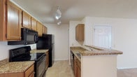 This single-floor residence offers a functional and comfortable layout with a thoughtful combination of finishes and features throughout. The galley-style kitchen is well-equipped, showcasing warm wood cabinetry, granite-style countertops, and a full suite of black appliances including a refrigerator, electric range, built-in microwave, and dishwasher. Track lighting illuminates the workspace, while light tile flooring adds a clean, cohesive look. A peninsula counter connects the kitchen to the adjoining living and dining area, which flows openly and benefits from a ceiling fan, a decorative chandelier, and a window that invites natural light and views of greenery outside. The living space is finished with the same neutral tile flooring, creating a bright and airy atmosphere. The bedrooms feature rich, dark hardwood-style flooring, neutral walls, and generous closet space with double bi-fold doors that reveal well-organized storage areas. The bathroom is highlighted by a wide granite-topped vanity with dual sinks, a large wall mirror, and ample cabinet storage below. Textured ceilings and consistent neutral tones throughout contribute to a cohesive, move-in-ready aesthetic across the entire space.