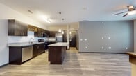This single-floor residence showcases a contemporary design highlighted by a well-appointed open-concept kitchen and living area. The kitchen is a standout feature, equipped with dark espresso cabinetry, granite countertops, and a full suite of stainless steel appliances including a French door refrigerator, electric range with over-the-range microwave, and dishwasher. A decorative wine rack cabinet adds a stylish touch, while a central granite-topped island provides additional workspace and casual seating. Pendant lighting and a track light fixture illuminate the kitchen, which flows seamlessly into the open living area over light-toned wood-look flooring.

The bedrooms feature neutral-toned carpet, ceiling fans with lighting, and windows fitted with horizontal blinds that allow natural light and exterior views. Dark-trimmed doors and baseboards provide a consistent design accent throughout.

The bathrooms maintain the same design language, featuring dark vanity cabinetry topped with granite countertops, large frameless mirrors, tub-shower combinations with tile surrounds, chrome fixtures, and wood-look flooring. The overall aesthetic throughout the space is clean, modern, and cohesive, with a neutral color palette and quality finishes.