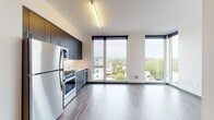 Located at 4030 N Williams Ave in Portland's vibrant Williams corridor, this modern single-floor unit offers a thoughtfully designed open-concept layout with clean lines and contemporary finishes throughout. Wide-plank hardwood-style flooring flows seamlessly across the living and kitchen areas, lending warmth and continuity to the space.

The living area is defined by striking floor-to-ceiling windows that frame sweeping views of the surrounding Portland neighborhood, flooding the interior with abundant natural light. The open kitchen is well-appointed with dark espresso cabinetry, light countertops with a tile backsplash, and a full suite of stainless steel appliances including a gas range, over-the-range microwave, dishwasher, and refrigerator.

A separate bedroom provides a quiet retreat, featuring its own window with natural light and direct access to a closet. The bathroom is finished with a dark wood vanity, stone-topped sink, and a clean, functional layout. A second bathroom is also present, accessible from the main living area.

Recessed linear lighting fixtures illuminate each room with a modern touch, while roller shades on the windows offer privacy and light control. The overall aesthetic is sleek and minimalist, making this a well-suited space for contemporary urban living in Portland.