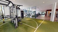 Located on Tresser Boulevard in Stamford, Connecticut, this large-scale fitness center spans a single floor offering a comprehensive and thoughtfully designed workout environment. The space is divided into distinct functional zones, each tailored to a specific training discipline.

A standout feature is the expansive artificial turf area, marked with lined court patterns and equipped with functional training stations, a multi-use cable rig, battle ropes, benches, and free weights — ideal for athletic and performance-based training. Flanking this zone is a broad hard-floor area with track-style striping, housing an extensive array of cardio machines including Peloton bikes, treadmills, and cycling equipment, all positioned along floor-to-ceiling glass walls that flood the space with natural light and offer open views of the surrounding greenery.

A dedicated strength training section features a comprehensive selection of selectorized machines, free weights, and cable stations. A separate stretching and functional movement area includes mirror walls, warm wood accent paneling, and ample open floor space for mat-based training.

Throughout the facility, tall concrete columns add an architectural character, while recessed lighting and white ceilings contribute to a bright, clean aesthetic. The abundance of natural light, generous proportions, and well-organized zones create a professional-grade fitness environment suited for a wide range of training needs.