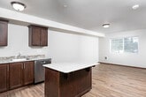 This single-floor residence offers a thoughtfully designed layout that balances functionality with modern style. The interior is finished with warm hardwood-style flooring throughout the main living and kitchen areas, complemented by rich dark wood baseboards and trim that add a refined contrast to the neutral white walls.

The kitchen is a standout feature, equipped with stainless steel appliances including a range, over-the-range microwave, and refrigerator. Rich dark wood cabinetry provides ample storage, while granite-style countertops with a subtle tile backsplash complete the polished look.

The living area is bright and open, with natural light filtering through window blinds, creating an airy and inviting atmosphere. Multiple bedrooms feature plush wall-to-wall carpeting and individual windows that bring in natural light and outdoor views, offering comfortable and versatile spaces.

The bathroom is well-appointed with a granite-topped vanity, dark wood cabinetry, and hardwood-style flooring, maintaining the consistent design language seen throughout the home. A dedicated in-unit laundry area with a stacked washer and dryer adds significant everyday convenience, as does the adjacent walk-in shower.

A hallway connects the various rooms seamlessly, with flush-mount lighting providing consistent illumination throughout. The overall ambiance is clean, modern, and move-in ready.