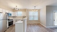 Located at 1638 Carlemont Dr in Crystal Lake, IL, this well-appointed 2-bedroom, 1-bathroom single-floor home offers a thoughtfully designed layout with modern finishes throughout. The open-concept kitchen and living area serves as the heart of the home, featuring crisp white shaker cabinetry, gleaming white quartz countertops, stainless steel appliances including a refrigerator, gas range, and microwave, and a peninsula with a built-in sink — all illuminated by a stylish chandelier. Natural light pours in through multiple windows fitted with blinds, creating a bright and welcoming atmosphere. The adjacent dining area is accented by its own pendant light fixture, making it ideal for everyday meals. Light-toned luxury vinyl plank flooring runs throughout the main living spaces, lending a clean, contemporary feel. Both bedrooms are carpeted for comfort, with large windows that invite plenty of natural light. The generously sized primary bedroom includes walk-in closet space outfitted with wire shelving systems for efficient organization. The full bathroom features a soaking tub with tiled surround and chrome fixtures. Two closets provide ample storage throughout the home, rounding out this practical and modern residence.