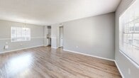 Located at 2002 Colonial Parc Dr in Tampa, FL, this one-bedroom, one-bathroom residence offers a well-organized layout across a single floor. The open living room greets you at the entry, featuring warm wood-look laminate flooring, neutral gray walls with white trim, and a textured ceiling that carries throughout the unit. A window at the front fills the space with natural light and offers views of the surrounding greenery. The adjoining dining area is defined by a pendant light fixture and an additional window, creating a pleasant spot for everyday dining. The kitchen is efficiently designed with white cabinetry, granite-style countertops, a double basin sink, and black appliances including a range and refrigerator. A window above the sink brings in additional natural light. The bedroom is a comfortable, well-proportioned room with the same wood-look flooring, soft gray walls, and a window overlooking the exterior. The full bathroom features a tiled tub-shower combination, a single vanity with a white basin, and a framed mirror. A hallway connects the main living areas to the bedroom and bathroom, contributing to the functional flow of the unit. Clean finishes and a consistent neutral palette give the space a cohesive, move-in ready feel.