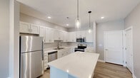 Located on Brook Boulevard in Sandusky, Ohio, this single-floor, 2-bedroom residence offers a well-designed layout with modern finishes and a bright, neutral color palette. The open-concept kitchen and dining area serves as the heart of the home, showcasing crisp white shaker-style cabinetry, light quartz countertops, a central island with pendant lighting, and a full suite of stainless steel appliances including a refrigerator, range, microwave, and dishwasher. Wood-look plank flooring runs throughout the main living areas, complementing the clean, contemporary aesthetic. The living area features vaulted ceilings, a ceiling fan, and a sliding glass door that fills the space with natural light. Both bedrooms are carpeted and include ceiling fans and windows that allow for ample daylight. The spacious primary bedroom offers a generous footprint, while each bedroom benefits from dedicated closet space — including a walk-in closet outfitted with wire shelving for organized storage. An additional area with wood-look flooring and wall sconce lighting provides flexible use. Throughout the residence, neutral gray walls, recessed lighting, and clean white trim contribute to a cohesive and move-in-ready atmosphere.