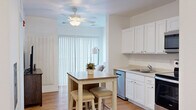 Located at 303 Airway Blvd in Belgrade, Montana, this one-bedroom, one-bathroom unit offers a well-designed single-floor layout that makes efficient use of every square foot. The open-concept kitchen is a standout feature, outfitted with stainless steel appliances including a range, microwave, refrigerator, and dishwasher, all complemented by crisp white cabinetry and light countertops. A compact dining area with a wooden table and stools sits adjacent to the kitchen, creating a natural flow for everyday living. Warm hardwood-style flooring runs throughout the main living areas, adding a cohesive and inviting feel. The living room is bathed in natural light through large sliding glass doors dressed with vertical blinds and shuttered panels, providing both brightness and privacy. The generously sized primary bedroom features plush carpeting, a large window with open views of the surrounding landscape, and dual sliding-door closets offering ample storage. The full bathroom is clean and functional, featuring a white vanity with storage, a combination shower and tub, and matching hardwood-style flooring. A stacked washer and dryer is conveniently tucked within the unit, adding everyday practicality. The overall aesthetic is bright, neutral, and modern throughout.