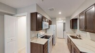 Located at 1252 Hillburn Ave NW in Grand Rapids, Michigan, this single-floor residence offers a functional and clean layout designed for comfortable everyday living. The galley-style kitchen is a standout feature, finished with rich dark wood cabinetry, light marbled countertops, and white appliances including a range, microwave, and refrigerator. A pass-through opening connects the kitchen to the main living area, enhancing the sense of openness throughout. The living room is carpeted and filled with natural light, courtesy of multiple windows and a glass door that frames views of surrounding greenery. The seamless connection between the living and dining areas creates an inviting, open flow. The bedrooms are carpeted and bathed in natural light through double windows overlooking the outdoors, offering a calm and comfortable atmosphere. The bathroom is neatly appointed with a tub-shower combination, sleek sliding glass enclosure, and light tile flooring. Neutral gray tones are carried throughout the unit's walls, contributing to a cohesive, modern aesthetic. Recessed lighting and in-unit laundry connections add practical value to this well-maintained space.