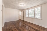 Located at 312 73rd St in Newport News, Virginia, this single-floor residence offers a well-organized layout with a variety of functional living spaces. Throughout the home, rich, dark-stained hardwood floors provide a warm and classic aesthetic, complementing the clean white walls and traditional trim details found in every room.

The living area is a standout space, featuring large multi-pane windows that allow generous natural light to fill the room and offer pleasant views of the surrounding greenery. A distinctive textured ceiling adds a layer of architectural character to the space. An additional room mirrors this charm with its own textured ceiling, hardwood floors, and direct access to other areas of the home.

The bedroom includes a closet for storage and continues the consistent hardwood flooring found throughout the residence. The kitchen is equipped with warm oak cabinetry, dark laminate countertops, a stainless steel sink, and white appliances including a range and over-the-range microwave, providing a practical and efficient cooking space. Tile flooring grounds the kitchen area.

The full bathroom features tile flooring, a full-size soaking tub with a shower, and a window that brings in natural light. White paneling and classic black accent tiling complete the bathroom's clean, timeless look. Overall, this home presents a cohesive and functional living environment with enduring design elements throughout.