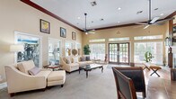 Located at 2900 Baby Ruth Ln in Nashville, TN, this single-floor community living space offers a generously sized, open layout designed for comfort and gathering. The space is defined by its soaring ceilings adorned with rich dark wood crown molding, recessed lighting, and ceiling fans that contribute to an airy, welcoming atmosphere.

The living area features a striking wood-framed fireplace with a slate tile surround and hearth, serving as a natural focal point. Warm hardwood flooring anchors the fireplace area, while plush carpeting extends throughout the main gathering zones. Large windows fitted with blinds, along with transom windows positioned high on the walls, flood the interior with abundant natural light.

A dining area with a wood table and upholstered chairs is seamlessly integrated into the space, connected to a tiled entryway featuring elegant double doors topped with an arched transom window. The lounge area is furnished with a comfortable sofa, glass-top coffee table, and tasteful wall art, creating an inviting setting.

French doors open directly to an outdoor pool area, bringing in views of the surrounding greenery and enhancing the connection between indoor and outdoor spaces. The overall ambiance is warm and classic, with traditional furnishings and architectural detailing that reflect a refined yet approachable character throughout.