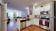 This single-floor residence is thoughtfully designed with a contemporary open-concept layout that seamlessly connects the kitchen, dining, and living areas. The kitchen is well-appointed with white shaker cabinetry, granite-style countertops, a full suite of stainless steel appliances including a gas range, microwave, refrigerator, and dishwasher. A peninsula with seating provides a natural gathering point and a smooth transition into the adjacent living space.

The living area is bright and welcoming, benefiting from large windows dressed with sheer curtains that invite natural light. Hardwood-style flooring runs throughout the main living spaces, adding warmth and visual continuity. The bedroom features plush carpeting, generous window placement offering ample natural light, and a closet, creating a comfortable and restful retreat. A second bedroom mirrors this layout with similarly sized windows and soft carpet underfoot.

The bathroom is finished with a white vanity, granite-style countertop, hardwood-style flooring, and a large mirror, contributing to a clean, modern aesthetic. Throughout the residence, neutral wall tones and recessed lighting complement the overall bright, contemporary ambiance.