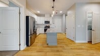 Located at 149 Main St in Upton, Massachusetts, this single-floor unit offers a well-designed, open layout with a thoughtful blend of modern finishes and comfortable living spaces. The kitchen serves as a standout centerpiece, featuring crisp white shaker cabinetry, granite countertops, a subway tile backsplash, and a full suite of stainless steel appliances including a gas range, microwave, dishwasher, and refrigerator. A central island with pendant lighting adds both functionality and style, while light hardwood flooring ties the kitchen and adjacent living areas together seamlessly. The living area benefits from natural light and features a sliding glass door that opens to a private balcony overlooking lush greenery. The bedrooms are finished with plush wall-to-wall carpeting and bright windows, creating a warm and restful atmosphere. The unit includes multiple bathrooms: one features a walk-in shower with built-in shelving and granite-topped vanity, while another offers a full soaking tub and shower combination with a similarly appointed vanity. Soft gray tones throughout the walls provide a clean, contemporary backdrop, complemented by white trim and modern fixtures. The overall ambiance is fresh, move-in ready, and well-suited for comfortable everyday living.