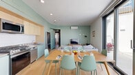 Located on S Barrington Avenue in the heart of West Los Angeles, this modern 5-bedroom, 3-bathroom unit offers a thoughtfully designed single-floor layout. The open-concept living, dining, and kitchen area serves as the heart of the home, characterized by warm light wood flooring, soft sage-green accent walls, and a curved architectural detail that defines the space with a contemporary flair. Large floor-to-ceiling sliding glass doors flood the living and dining areas with abundant natural light and open to views of the surrounding courtyard. The kitchen features light wood cabinetry, white tile backsplash, stainless steel appliances including a French door refrigerator and dishwasher, and sleek countertops. The living area is equipped with a wall-mounted mini-split system for year-round comfort. The five bedrooms are clean and minimalist, each featuring white walls, wood flooring, built-in closets, and frosted glass interior doors that add a modern touch while maintaining privacy. The three bathrooms are finished in crisp white with sage-green floors, tiled shower stalls, and simple chrome fixtures. A connected hallway ties all rooms together efficiently, making the layout highly functional for shared or multi-occupant living.