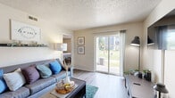 Located at 1301 W 24th St in Lawrence, Kansas, this 2-bedroom, 2-bathroom unit offers a functional and well-appointed single-floor layout. Wood-style flooring runs throughout, lending a cohesive and clean aesthetic to every room.

The living room is a welcoming space anchored by a sliding glass door that fills the area with natural light and provides views of the surrounding grounds. The open layout comfortably accommodates a seating area and media setup, making it ideal for both relaxing and entertaining.

The kitchen is efficiently designed with two-tone cabinetry — white upper cabinets paired with gray lower cabinets — complemented by light countertops and a full suite of stainless steel appliances, including a refrigerator, range, microwave, and dishwasher. A ceiling fan adds comfort to the space.

Both bedrooms are well-sized, with the primary bedroom offering a window with outdoor views and ample room for a full bedroom set. The second bedroom also features a window and includes space for a desk, making it versatile as a guest room or home office. Each bedroom is served by its own full bathroom, both featuring tub/shower combinations and wood-style flooring. A hallway connects the rooms, completing this efficiently organized and comfortable home.