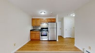 Located at 135 Ward St in Revere, Massachusetts, this single-floor residence offers a practical and well-appointed layout designed for comfortable everyday living. The open-concept kitchen and living area serves as the heart of the unit, where warm honey-toned wood cabinetry pairs with a stylish mosaic tile backsplash, dark granite-style countertops, and a full suite of stainless steel appliances — including a refrigerator, electric range with oven, and an under-cabinet range hood. Light hardwood flooring anchors the kitchen area and transitions seamlessly into the carpeted living space, which is generously proportioned and features baseboard heating along the perimeter. A wall-mounted air conditioning unit and sliding door access add to the comfort and functionality of the living area. The bedroom is a calm, carpeted retreat with ample room for furnishings, a built-in closet for storage, and continued baseboard heating. The bathroom is clean and bright, finished with a white soaking tub and shower surround accented by chrome fixtures. Throughout the unit, neutral wall tones and crisp white trim create a bright, cohesive aesthetic that is both inviting and move-in ready.