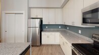 Located at 257 Broadway St in the heart of Asheville, NC, this single-floor unit offers a well-designed, open-concept layout with thoughtful finishes throughout. The kitchen is a standout feature, showcasing white cabinetry that extends to the ceiling for ample storage, granite countertops, a teal tile backsplash, and a full suite of stainless steel appliances including a refrigerator, range, and microwave. A central island with pendant lighting and an integrated sink adds both functionality and visual appeal, seamlessly connecting the kitchen to the main living area. The living space is bright and airy, benefiting from natural light that streams through a sliding glass door leading to a private balcony with outdoor views of surrounding greenery. Light wood-style flooring runs throughout the main areas, while the bedroom features plush carpeting and dual windows that invite additional natural light. The bathroom is finished with granite countertops, a single-sink vanity, tile flooring, and a separate water closet. A ceiling fan, generous ceiling height, and neutral warm tones throughout contribute to a comfortable and cohesive living environment.
