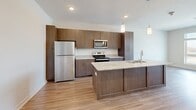 This thoughtfully designed one-bedroom, one-bathroom unit offers a contemporary open-concept layout that maximizes its efficient footprint. The combined kitchen and living area serves as the heart of the space, where light wood-style plank flooring extends throughout, creating a cohesive and airy atmosphere. The kitchen is well-appointed with rich dark wood cabinetry reaching toward the ceiling, providing ample storage. A central island with a granite countertop and undermount sink doubles as a breakfast bar, while stainless steel appliances—including a refrigerator, electric range, and microwave—complete the modern aesthetic. Pendant lighting above the island adds a refined touch. The open living area benefits from a large window that invites natural light and outdoor views.

The bedroom features soft wall-to-wall carpeting, a ceiling fan, and a bright window overlooking the surrounding landscape. A dedicated closet provides organized storage. The bathroom continues the upscale finishes with a granite-topped vanity, light wood cabinetry, an undermount sink, and a large mirror. Clean white walls and neutral tones throughout the unit contribute to a bright, move-in-ready ambiance.