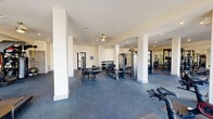Located at 1880 Maple Dr NW in Kennesaw, Georgia, this well-appointed fitness center offers a generously sized, single-floor exercise space designed to accommodate a wide range of workout needs. The open floor plan is anchored by white structural columns that define separate workout zones without interrupting the overall sense of openness. Durable rubber-composite flooring covers the entire space, providing both safety and comfort underfoot.

The strength training area is thoroughly equipped with multiple cable and weight machines, a dumbbell rack, a power rack, and adjustable benches, supporting everything from isolation exercises to full compound movements. The cardio section features rowing machines, upright and spin bikes, and treadmills, lined along the perimeter to maximize floor space. Full-length mirrors along one wall enhance the sense of depth and allow users to monitor form.

Large windows along the exterior walls usher in abundant natural light, contributing to a bright and motivating atmosphere. Recessed ceiling lighting and a ceiling fan ensure consistent illumination and air circulation throughout. The clean, white walls and neutral tones create a crisp, professional environment. The facility is accessible via glass-paneled entry doors and includes clearly marked emergency exits, reflecting a strong emphasis on safety and functionality.