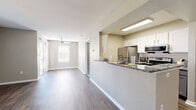 This two-floor residence offers a thoughtfully designed layout with a blend of modern finishes and functional living spaces throughout. The main level centers around an open-concept kitchen and living area, where a peninsula with granite countertops and a built-in sink provides a natural gathering point. The kitchen is equipped with stainless steel appliances, white upper cabinetry, and gray lower cabinets, all complemented by wood-look flooring that extends seamlessly into the living area. The living room benefits from natural light streaming through a sliding glass door that opens to a private balcony, and a ceiling fan adds comfort overhead. A full bathroom on this level features a granite-topped vanity with gray cabinetry and a tub-shower combination. The upper level hosts generously sized bedrooms, each showcasing dramatic vaulted ceilings that lend an airy, open feel. These rooms are finished with plush carpet flooring and feature windows with blinds that invite natural light. Ample closet storage is provided via sliding-door closets. A second full bathroom serves the upper level with wood-look flooring and a shower-tub unit. A dedicated laundry room with a full-size washer and dryer, along with overhead shelving, adds practicality to the home.