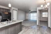 This single-floor unit is designed with a practical, open-concept layout that connects the kitchen and living area into one cohesive space. The kitchen features dark espresso cabinetry, a peninsula with a double stainless steel sink and light countertops, a black refrigerator, and black appliances including a range and over-the-range microwave. A pendant light fixture above the peninsula adds focused task lighting, while wood-look plank flooring runs throughout the kitchen and entry areas.

The living area transitions from the hard flooring to plush carpeting, creating a defined and comfortable space. A ceiling fan overhead and a large sliding glass door with vertical blinds allow natural light to enter and provide outdoor access. A wall-mounted HVAC panel is centrally located in the living room. The dining area features wood-look flooring and is highlighted by a chandelier, with an electrical panel recessed into the wall.

The bedroom is carpeted, with a sliding window that brings in natural light and views of the surrounding landscape. The bathroom includes tile-look flooring, a tub-shower combination, a toilet, and a dark-cabineted vanity with a light countertop and mirror. Textured ceilings are present throughout the unit.