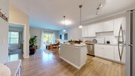 Located at 9 Covered Bridge Rd in Newtown, CT, this well-appointed one-bedroom, one-bathroom residence offers a thoughtfully designed single-level layout. The open-concept kitchen and living area serves as the heart of the home, featuring a central island with granite countertops, white shaker cabinetry, a teal subway tile backsplash, stainless steel appliances, and pendant lighting with crown molding accents. Hardwood-style flooring flows seamlessly throughout the space, adding warmth and continuity. The living room is bright and inviting, benefiting from a large sliding glass door that opens to a private balcony overlooking lush, mature trees — an ideal spot for outdoor relaxation. The bedroom is a comfortable retreat, offering natural light through a large window with wooded views, and ample space for a full furniture arrangement. The bathroom is well-finished with a dark wood vanity, white countertop, large mirror, and a full tub-shower combination with crown molding detail. A built-in entry bench with hooks provides convenient storage near the front door, adding a practical touch to this cozy yet functional Newtown residence.