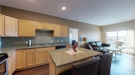This single-floor unit at 2303 Shoal Loop SE in Mandan, North Dakota offers a practical and comfortable layout designed for everyday living. The kitchen is a standout feature, outfitted with light maple cabinetry, granite countertops, stainless steel appliances including a refrigerator, gas range, built-in microwave, and dishwasher, along with a central island with bar seating — ideal for casual dining. Wood-look flooring runs throughout the kitchen and living areas, adding warmth and continuity. The open living room flows naturally from the kitchen, providing generous space for seating and relaxation, and is highlighted by a sliding glass door that opens to a private balcony with outdoor views. Two bedrooms offer carpeted flooring and natural light from well-positioned windows, with one bedroom featuring a view of the surrounding neighborhood. The unit includes two full bathrooms, each with wood-look flooring, granite-topped vanities with light maple cabinetry, and a tub/shower combination. A dedicated in-unit laundry area with a washer and dryer adds further convenience. Neutral wall tones and recessed lighting throughout create a clean, welcoming atmosphere suited for a variety of lifestyles.
