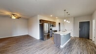 This single-floor unit offers a thoughtfully designed open-concept layout that seamlessly connects the kitchen, dining, and living areas. The kitchen serves as a central hub, anchored by a large island with a quartz countertop and double undermount sink, illuminated by stylish pendant lighting. Dark-toned cabinetry pairs with a full suite of stainless steel appliances, including a French door refrigerator, electric range, and built-in microwave. Wood-look plank flooring extends throughout the main living areas, adding warmth and continuity.

The living area is generously sized, featuring a ceiling fan, a wall-mounted mini-split system for climate control, and access to a sliding door leading outside. A bedroom offers plush carpeting, a window with an outdoor view, and a dedicated mini-split unit. A spacious walk-in closet with wire shelving provides ample storage.

Two bathrooms are finished with dark wood vanities, quartz countertops, large mirrors, and wood-look flooring. One bathroom includes a full tub-shower combination. The unit also features in-unit laundry hookups, completing this well-appointed, modern living space.